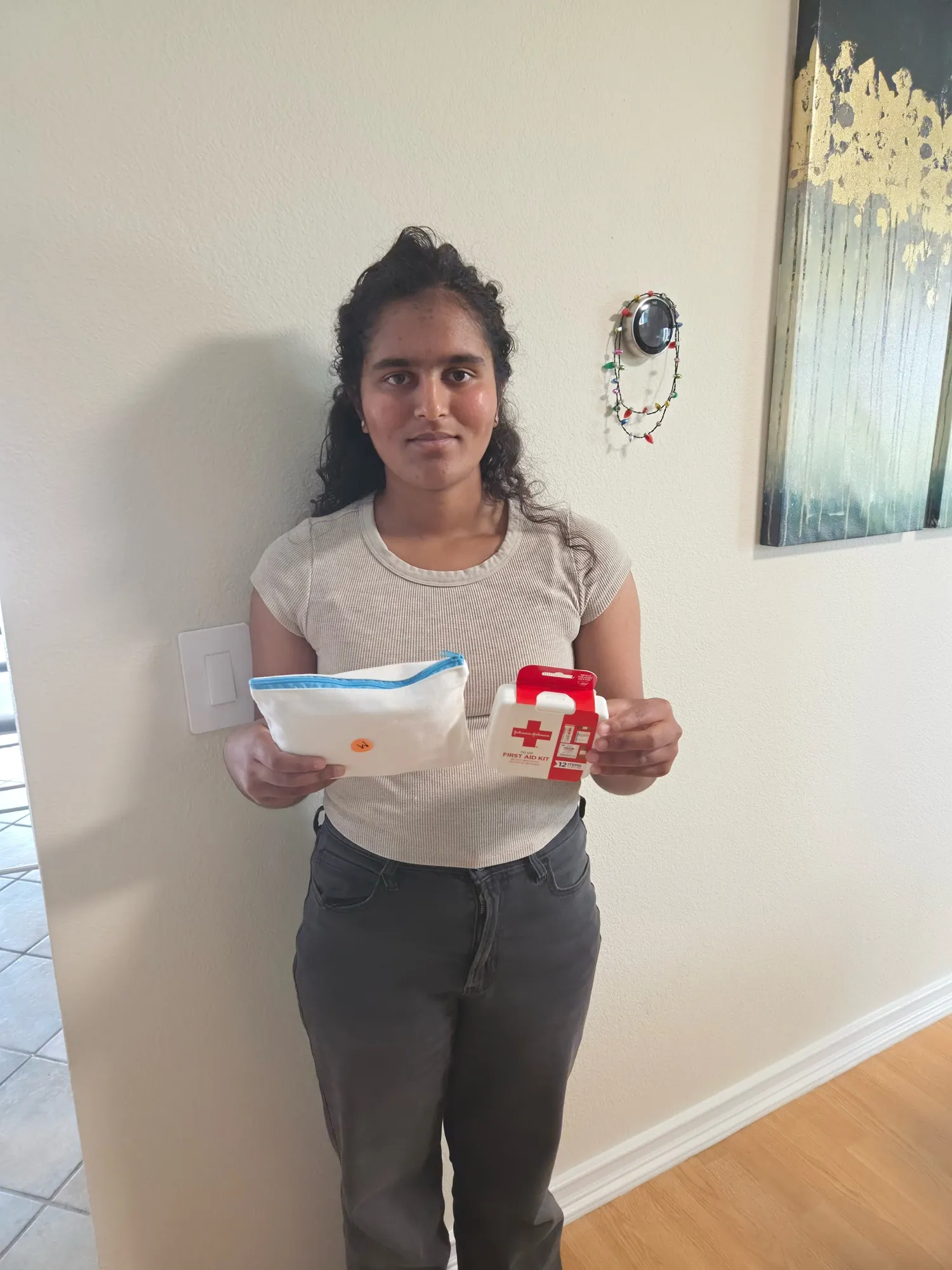 Isha holding a finished hygiene pouch in one hand and a ready-made first aid kit in the other.