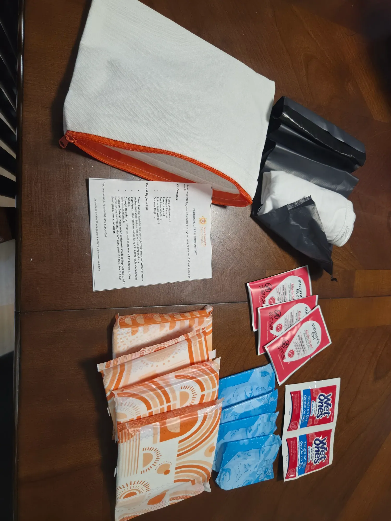 The contents of one hygiene kit laid out: a zippered canvas pouch, pads, wipes, disposal bags, and a printed care card.