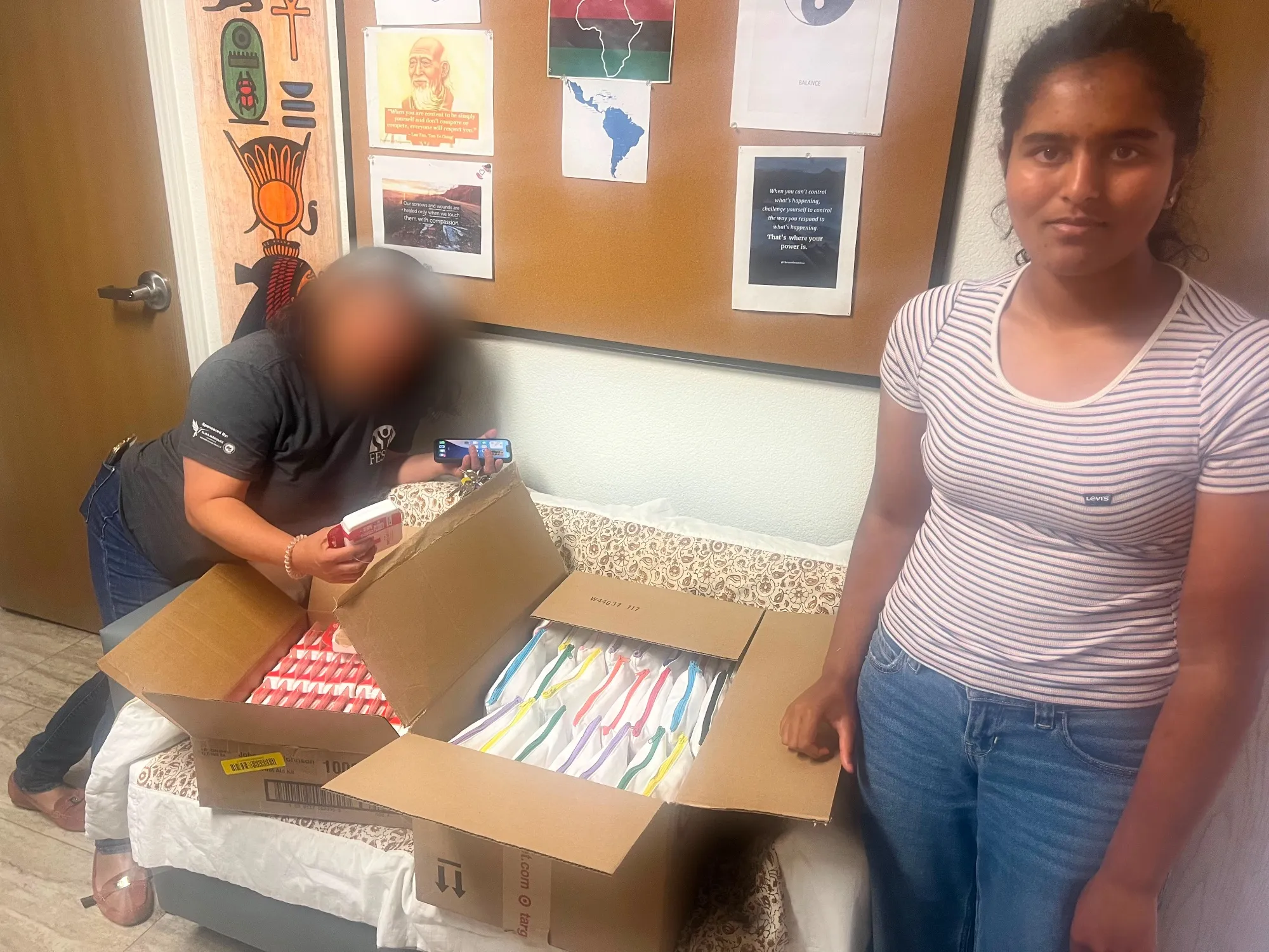 Boxes of toothbrushes and supplies opened on a bed in a shelter room, with a staff member sorting through them.